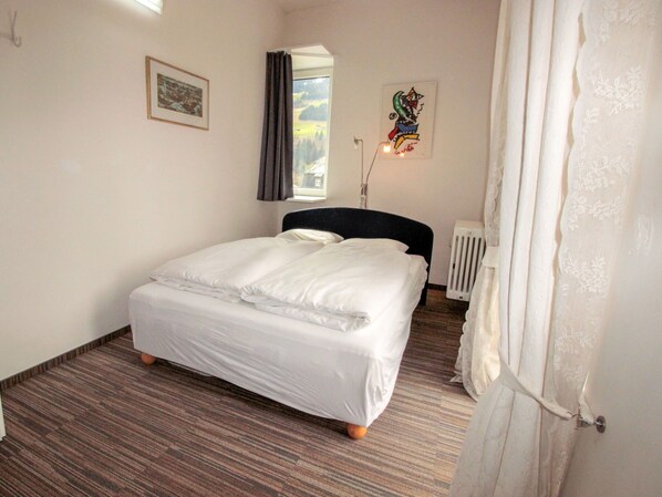 A bedroom with a bed, a radiator, a window with curtains, and a painting on the wall. - Apartment Kern by Interhome (Bad Hofgastein)
