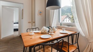 Comedor con una mesa de madera, sillas, una lámpara colgante negra y una ventana con vistas a montañas.