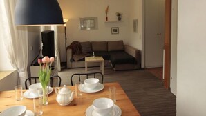 Un comedor con una mesa de madera dispuesta para tomar té, una lámpara negra y un sofá al fondo.