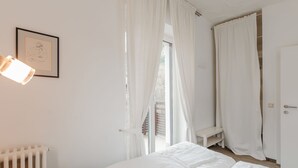 Un dormitorio con cama, radiador, un cuadro enmarcado y ventana con cortinas.