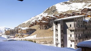A snow-covered mountain with wooden buildings, including a large hotel with balconies and a ski lift visible in the background.