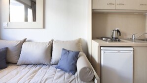 A compact hotel room with a bed, a kitchenette, and a mirror on the wall.