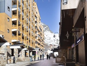 Un immeuble à plusieurs étages, doté de balcons et d’une façade en pierre, avec une chaîne de montagnes en arrière-plan.