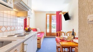 A compact kitchen with a stove, sink, and a dining area with a table and chairs. - Chalet Club (Val Claret) by Interhome (Tignes)