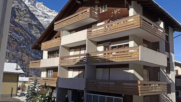 A multi-story hotel with balconies, a ski slope in the background, and snow on the ground. - Apartment Castor by Interhome (Täsch)