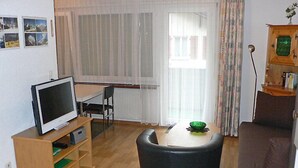 A living room with a television on a wooden stand, a dining table with chairs, a brown sofa, and a window with curtains. - Apartment Castor by Interhome (Täsch)