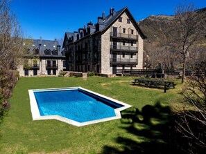 Ein großes Steinhaus mit mehreren Balkonen, einem Pool und Picknicktischen auf einer Rasenfläche.