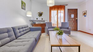 Un soggiorno moderno con un divano grigio, due poltrone, un tavolino in legno e un angolo cottura con fornello e pensili.