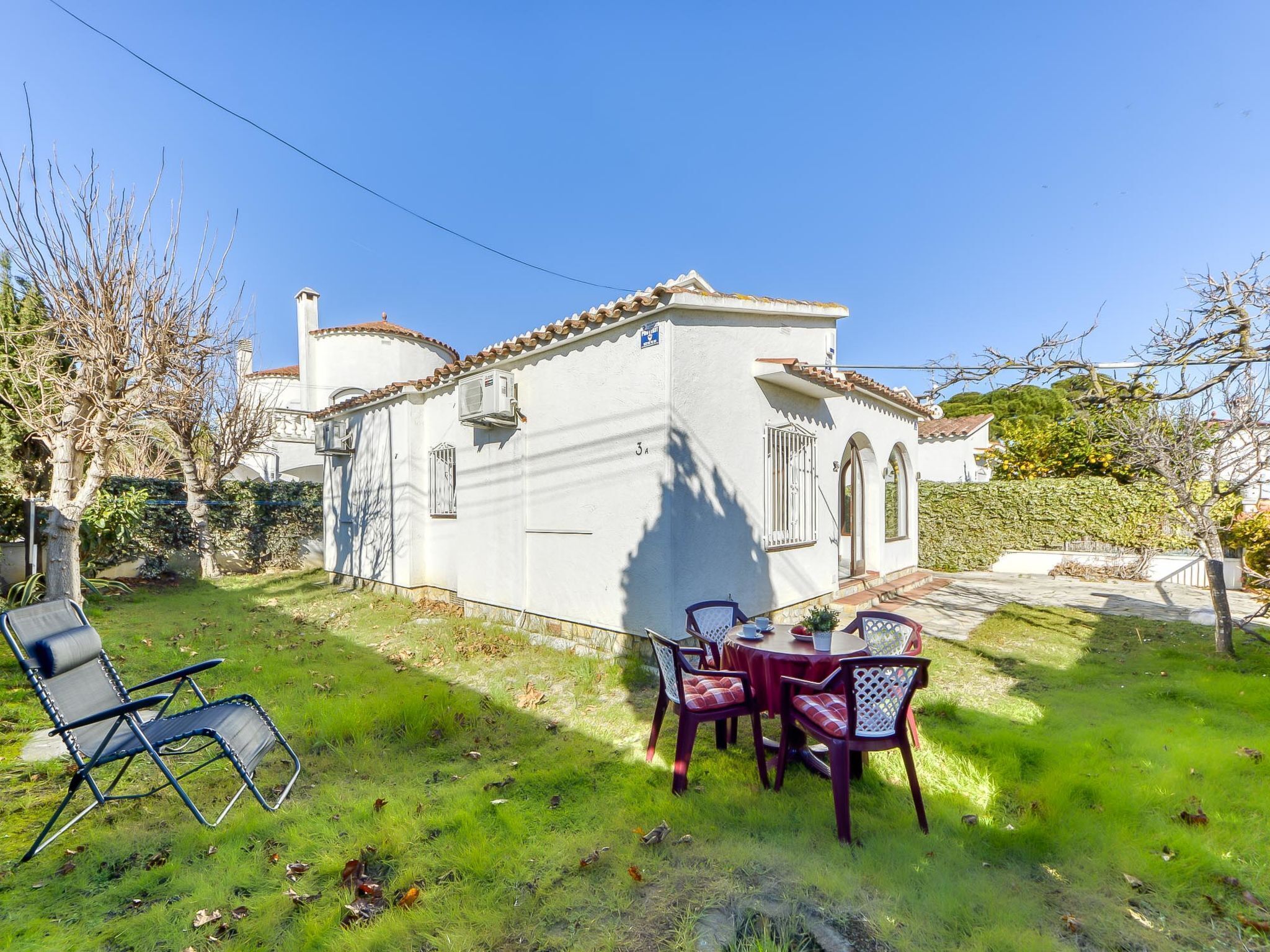A white building with a tiled roof, a small patio with a table and chairs, and a grassy yard.