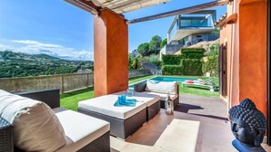 A rooftop terrace with outdoor seating, a pool, and a view of the surrounding landscape.