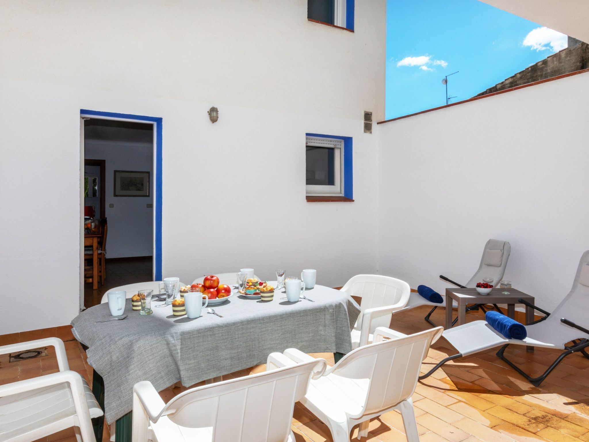 A dining area with a table set for four, surrounded by white chairs, a blue-framed window, and a view of the sky.