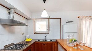 A kitchen with a gas stove, sink, wooden cabinets, a stainless steel range hood, and a window. - Delta 1 by Interhome (L'Escala)