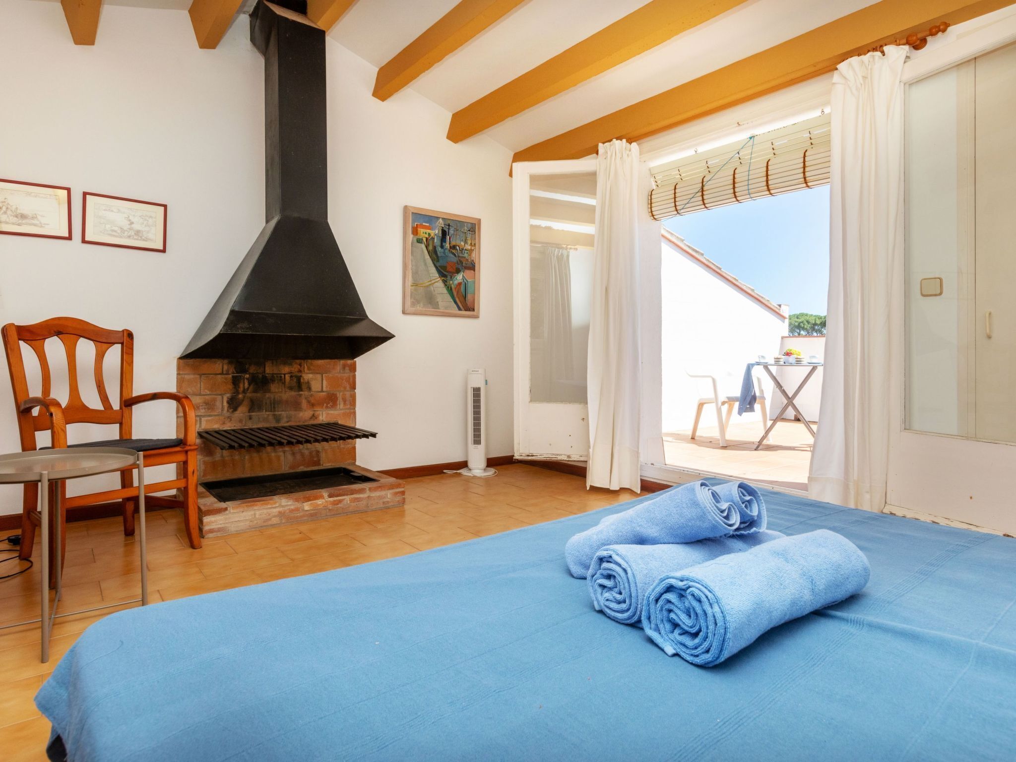 A room with a bed, a fireplace, a chair, and a view to an outdoor area.