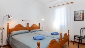 A double bed with wooden headboards, two bedside lamps, a chair, and a poster on the wall. - Delta 1 by Interhome (L'Escala)