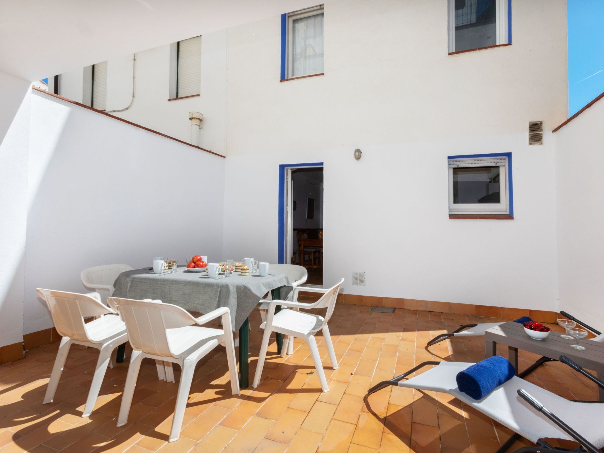 A patio with a table set for dining, surrounded by white chairs.
