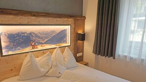 A hotel room with a wooden headboard, a large framed picture of a mountain landscape, white bedding, and a bedside lamp. - Apartment Ladis by Interhome (Fiss)