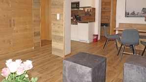 A modern living space with wooden walls, a kitchen area, and a dining area with grey chairs. - Apartment Ladis by Interhome (Fiss)