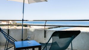 Un balcón con mesa y sillas, una sombrilla y vista a la playa y el océano.