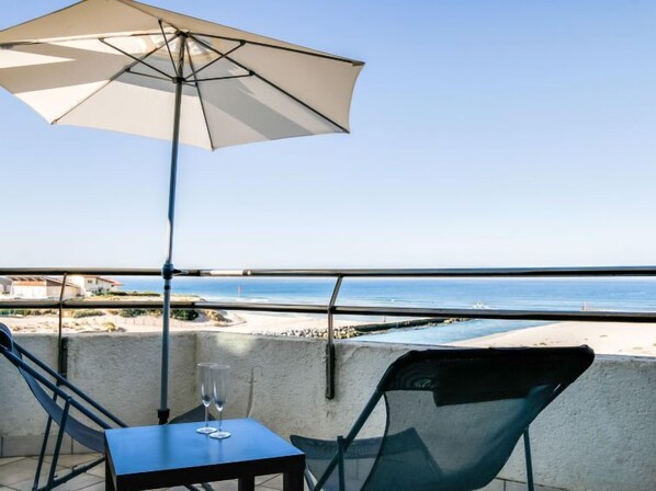 Ein Balkon mit Tisch, Stühlen und Sonnenschirm, mit Blick auf Strand und Meer.