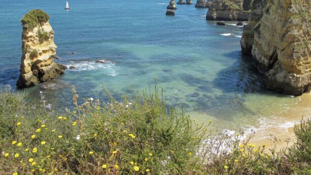 A coastal landscape with clear waters, rocky formations, and a sailboat in the distance. - Rua 5 de Outubro by Interhome (Lagos)