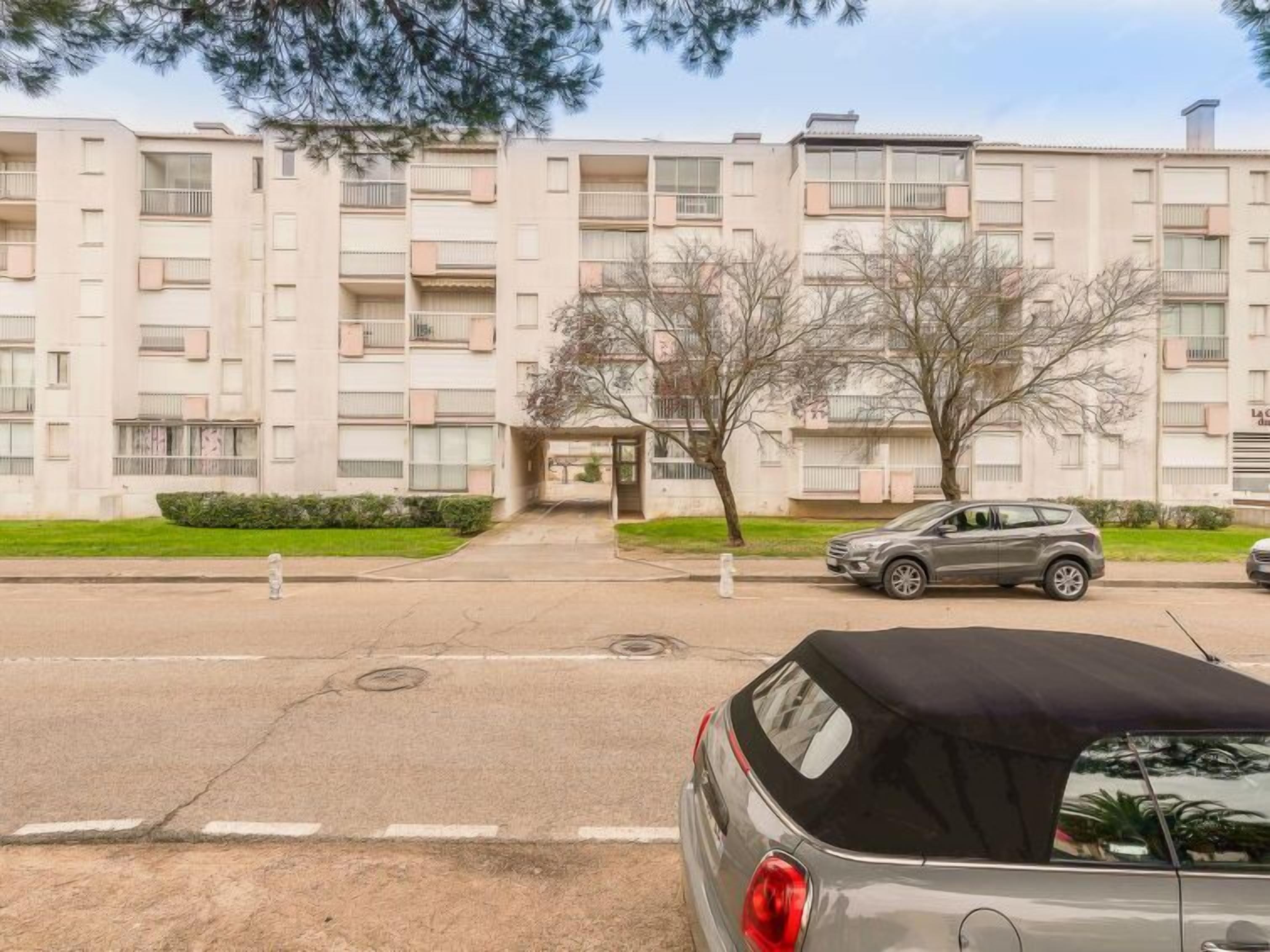 A multi-story residential building with a central entrance, a parking area, and a car parked in front.