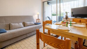 Ein modernes Wohnzimmer mit einer Couch, einem Esstisch, Stühlen, einem Fernseher und einem großen Fenster.