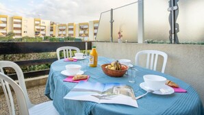 Ein Tisch ist für ein Frühstück auf einem Balkon gedeckt, im Hintergrund ist ein Gebäude zu sehen.
