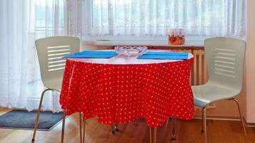 A dining area with a round table covered in a red polka dot tablecloth, two chairs, and a window with sheer curtains.