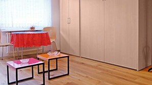 Una habitación con piso de madera, una mesa con mantel rojo, una silla y un armario grande.