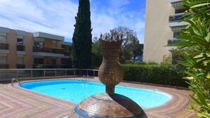 Una piscina con una fuente de mosaicos en el centro, rodeada por un solárium con baldosas.