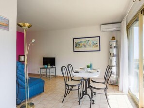 A dining area with a round table and four chairs, a sofa, a TV, and a painting on the wall.