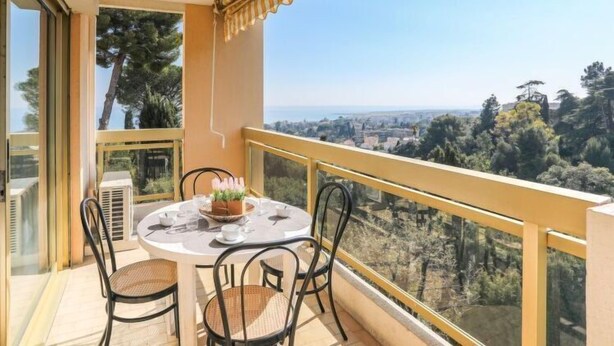 Un balcón con una mesa para dos, con vistas a un paisaje urbano y áreas verdes.