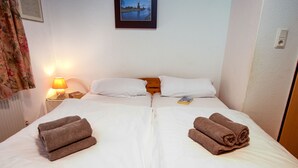 A double bed with white linens, two rolled towels, a bedside lamp, and a framed picture on the wall. - Windrad by Interhome (Norddeich)