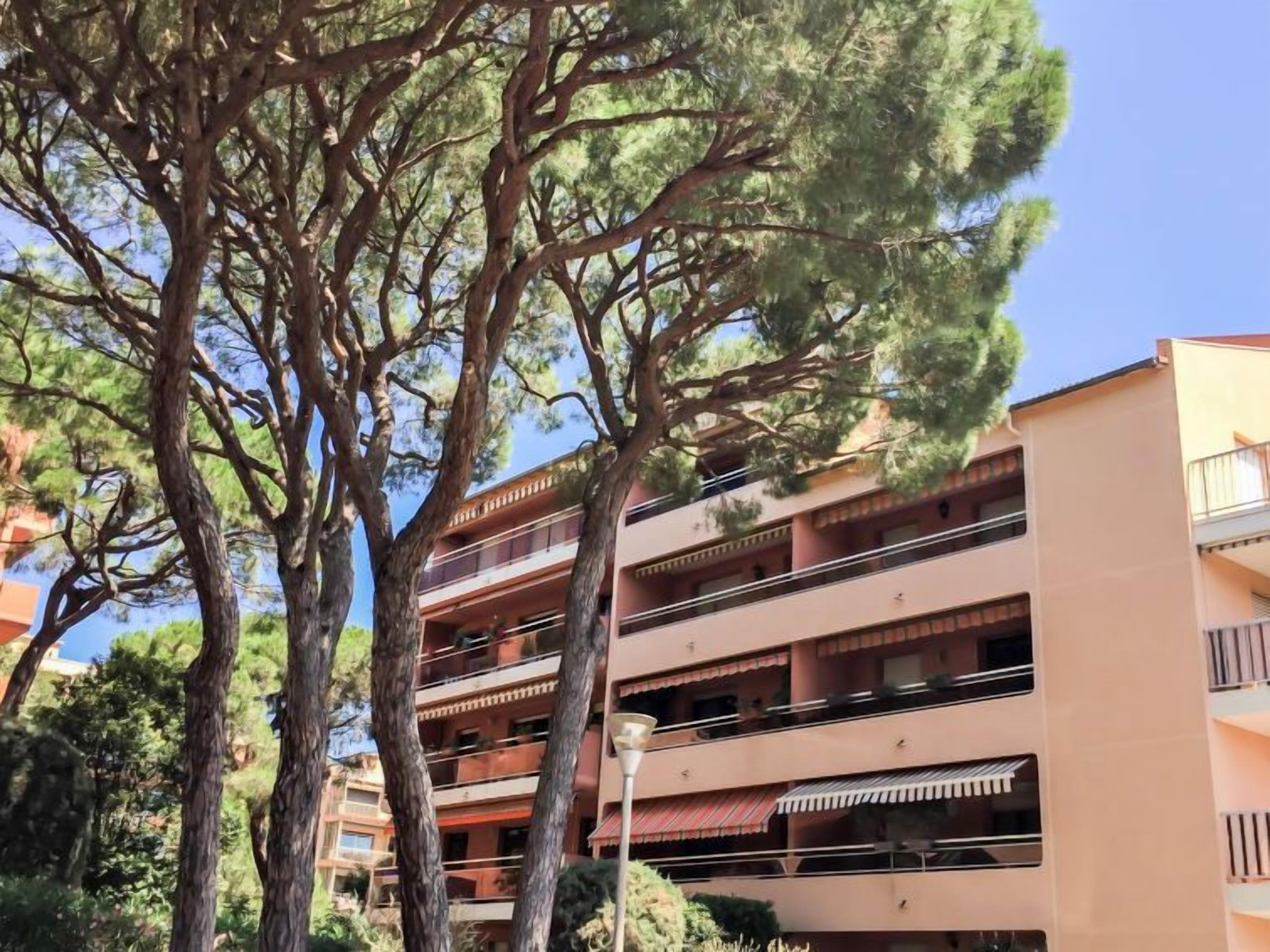 A multi-story building with balconies, surrounded by trees.