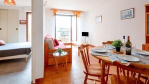 A dining area with a wooden table set for two, a television on a stand, and a view of the outside through a large window. - Les Pins Ensoleilles by Interhome (Sainte Maxime)