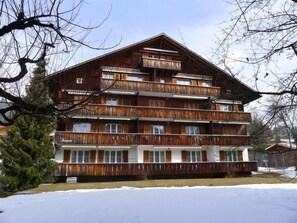 Un edificio in legno a più piani con balconi, circondato da neve e alberi.