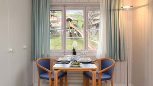 A dining area with a table set for two, a window with a view of a playground, and a floor lamp. - Suzanne Nr. 21 by Interhome (Schönried)