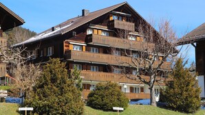 A multi-story wooden building with balconies, surrounded by trees and a clear sky. - Suzanne Nr. 21 by Interhome (Schönried)