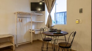 A compact room with a small table and two chairs, a TV mounted on the wall, and a window with curtains. - Casa Isza (Playa del Carmen)