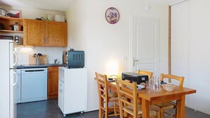 A compact kitchen with wooden cabinets, a refrigerator, a toaster, and a dining table with chairs. - Les erables by Interhome (Saint Gervais)