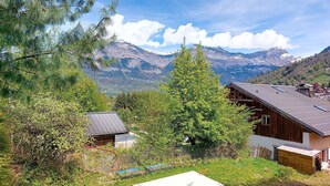 A wooden cabin with a sloped roof, surrounded by lush greenery and a mountainous backdrop. - Les erables by Interhome (Saint Gervais)