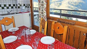 Een eetgedeelte met een tafel voor vier personen, een keuken op de achtergrond en een uitzicht op een bergachtig landschap door een raam.