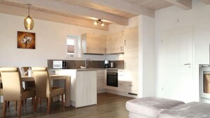Een moderne keuken met witte kasten, een eethoek met een tafel en stoelen, en een grijze bank.