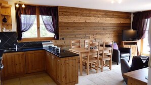 Een compacte keuken met houten kastjes, een eethoek met tafel en stoelen, en een televisie.