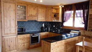 Een keuken met houten kastjes, een zwart aanrecht, een inbouwoven en een raam met gordijnen.