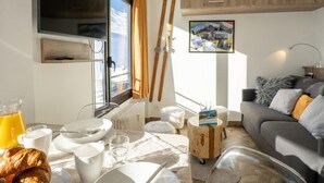 A modern living room with a sofa, a coffee table, and a dining area with plates and a croissant. - Les Tufs (Val Claret) by Interhome (Tignes)