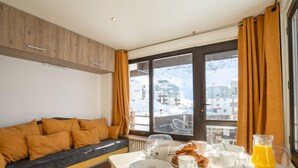 A modern hotel room with a sofa, breakfast table, and a view of snowy buildings. - Les Tufs (Val Claret) by Interhome (Tignes)