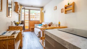 Une pièce chaleureuse avec un bureau en bois, une petite table où sont disposés des articles pour le petit-déjeuner, un canapé et une vue sur un bâtiment par la fenêtre.