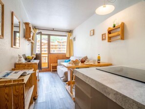 A cozy room with a wooden desk, a small table with breakfast items, a sofa, and a view of a building through a window. - vanoise 578 by Interhome (Val Thorens)