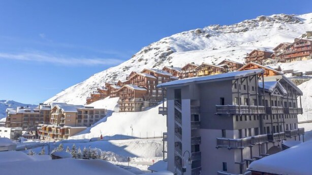 Une montagne enneigée, parsemée de chalets en bois et surmontée d’un bâtiment moderne doté de balcons.